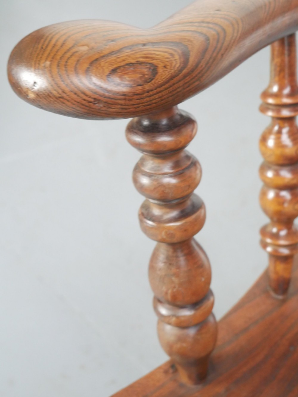 An antique wooden Windsor armchair with a hoop back, central pierced splat, spindle backrest, broad armrests, and turned legs with an H-stretcher in a warm brown timber finish. View VI