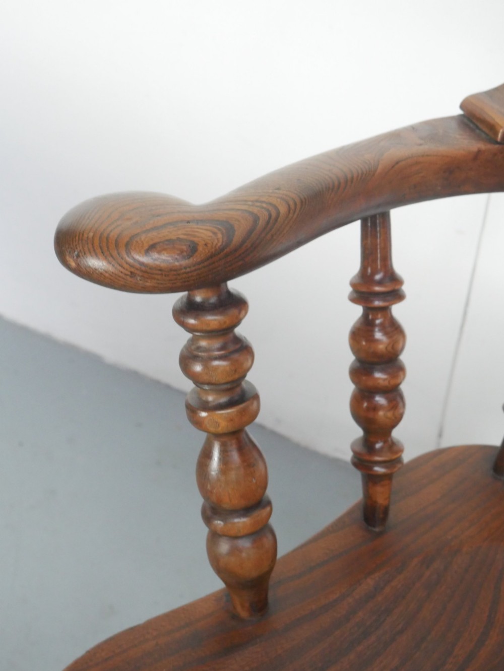 An antique wooden Windsor armchair with a hoop back, central pierced splat, spindle backrest, broad armrests, and turned legs with an H-stretcher in a warm brown timber finish. View VII