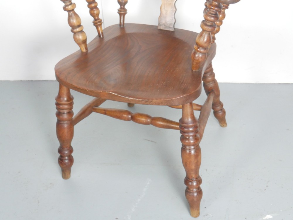 An antique wooden Windsor armchair with a hoop back, central pierced splat, spindle backrest, broad armrests, and turned legs with an H-stretcher in a warm brown timber finish. View VIII