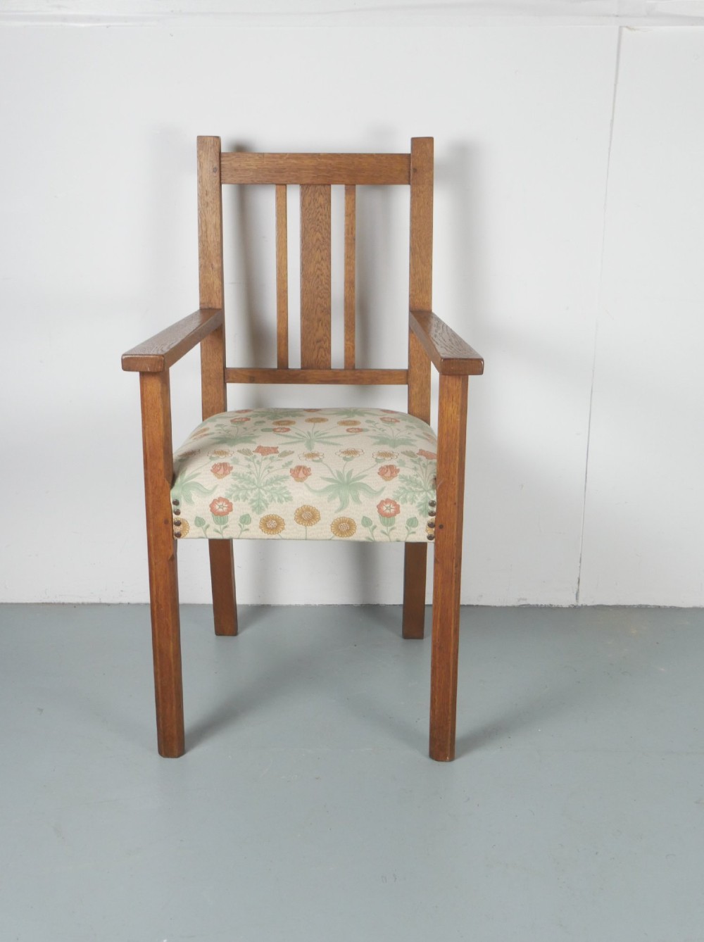 An Arts and Crafts style medium oak armchair featuring vertical back slats, flat armrests, and floral pattern upholstery with brass stud trim. View V