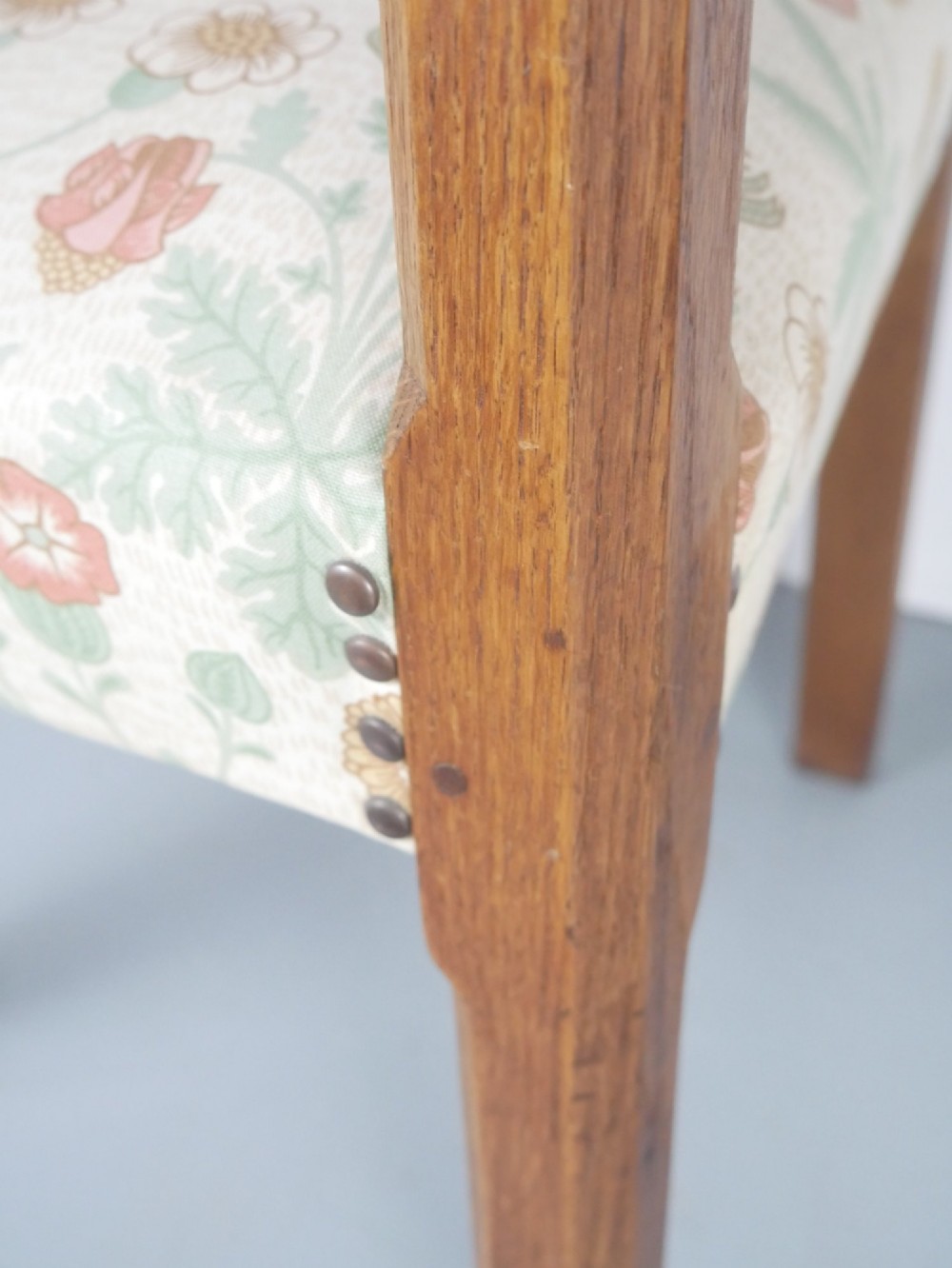 An Arts and Crafts style medium oak armchair featuring vertical back slats, flat armrests, and floral pattern upholstery with brass stud trim. View VI