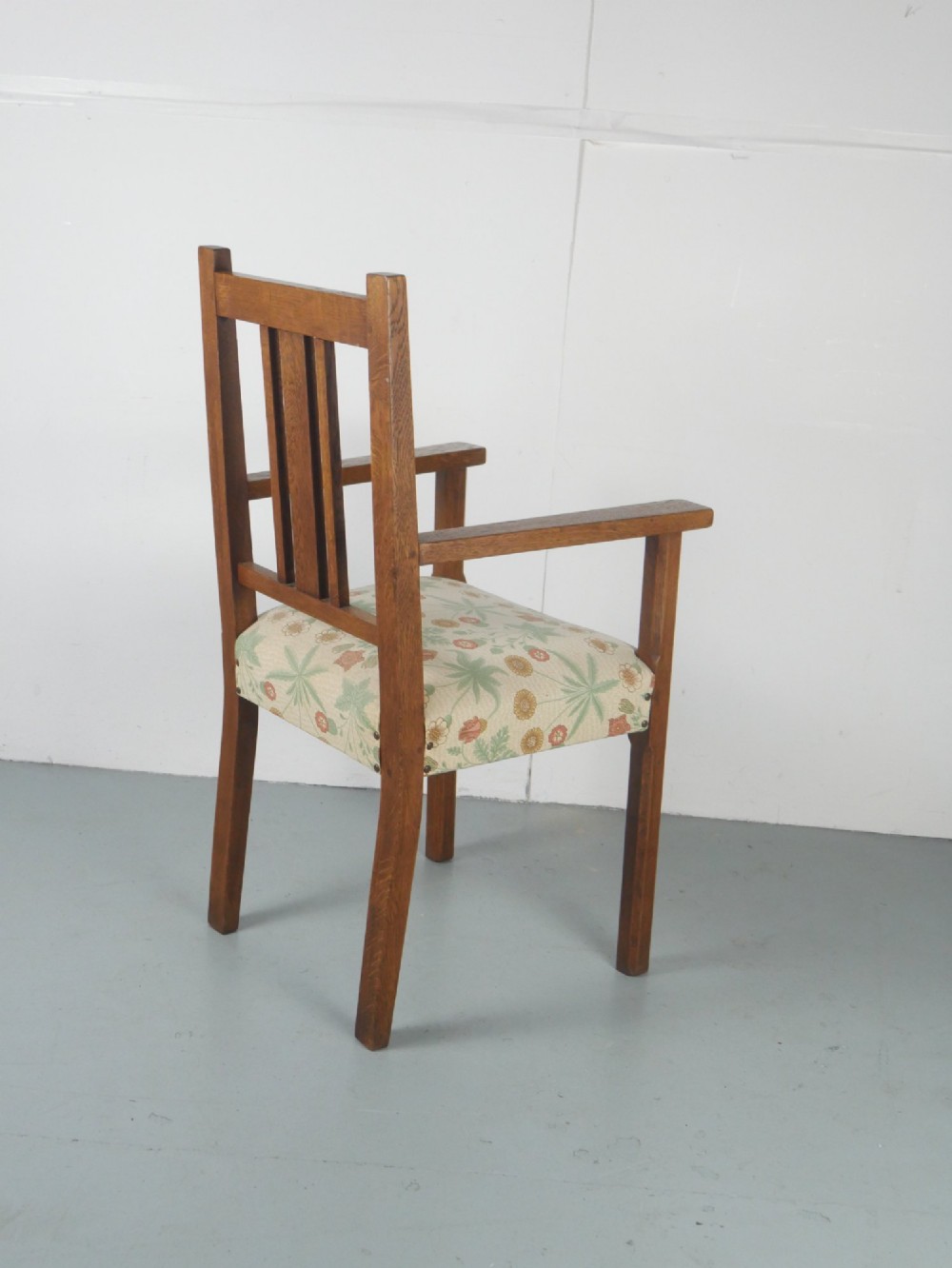 An Arts and Crafts style medium oak armchair featuring vertical back slats, flat armrests, and floral pattern upholstery with brass stud trim. View VIII