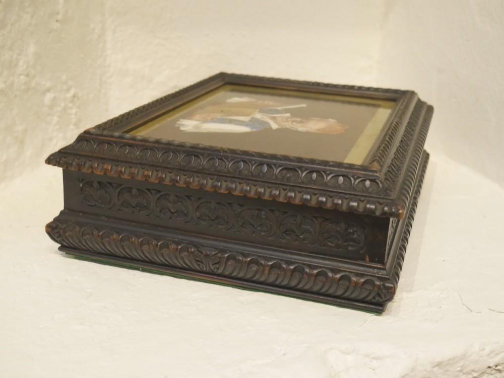 A rectangular dark carved wooden box featuring a detailed pietra dura hardstone inlay depicting an elderly man in spectacles reading a book. View VI