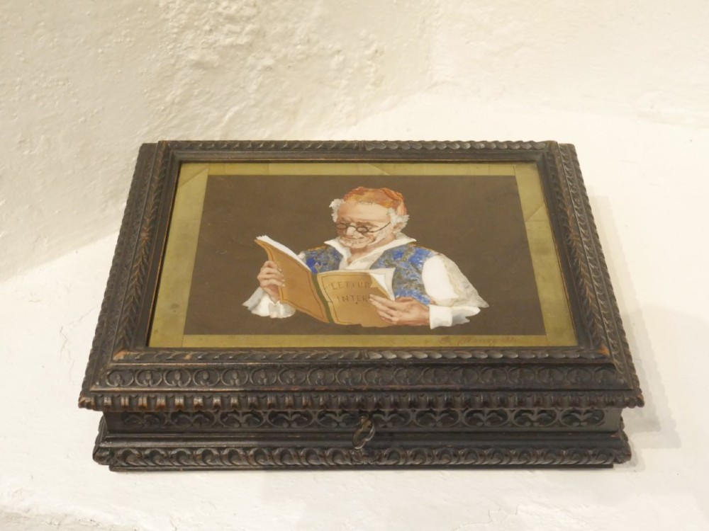 A rectangular dark carved wooden box featuring a detailed pietra dura hardstone inlay depicting an elderly man in spectacles reading a book. View IX