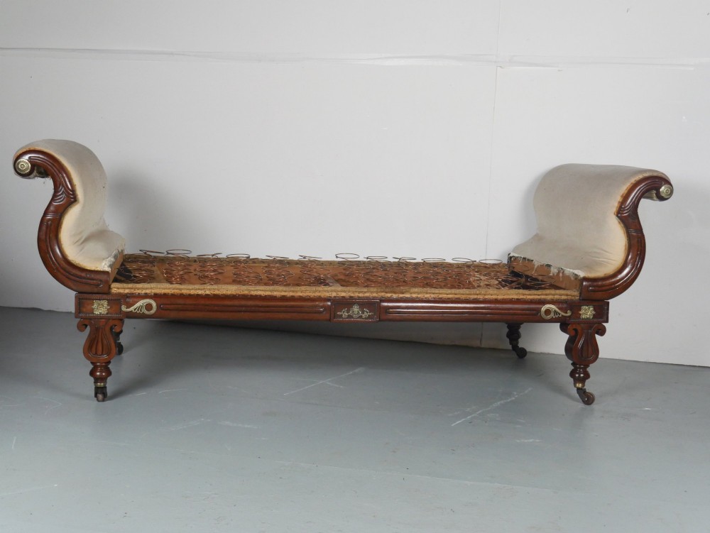 An early nineteenth-century Regency mahogany scroll-ended sofa frame featuring brass mounts, reeded turned legs on brass castors, and upholstered end scrolls with exposed spring seating.