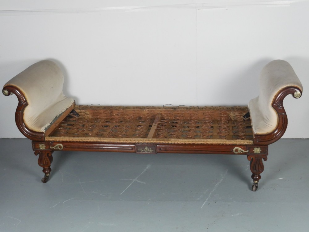 An early nineteenth-century Regency mahogany scroll-ended sofa frame featuring brass mounts, reeded turned legs on brass castors, and upholstered end scrolls with exposed spring seating. View II