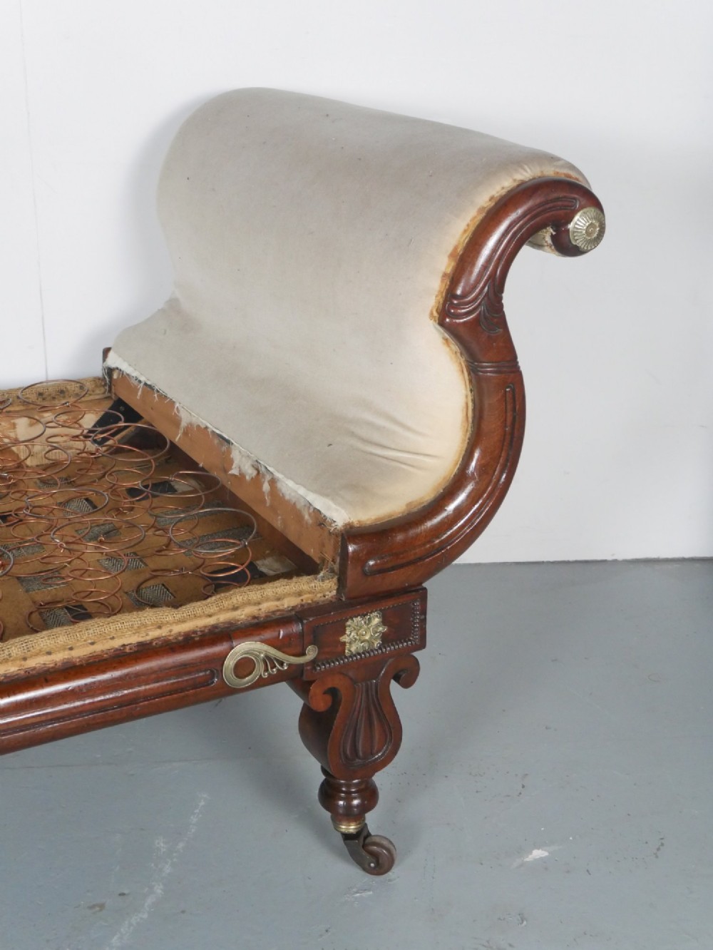 An early nineteenth-century Regency mahogany scroll-ended sofa frame featuring brass mounts, reeded turned legs on brass castors, and upholstered end scrolls with exposed spring seating. View III