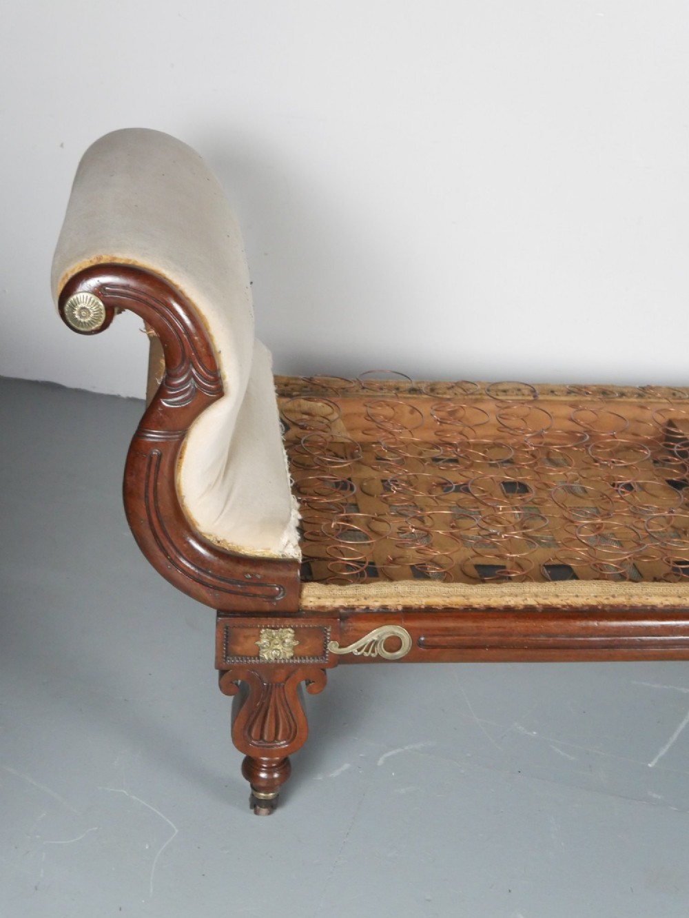 An early nineteenth-century Regency mahogany scroll-ended sofa frame featuring brass mounts, reeded turned legs on brass castors, and upholstered end scrolls with exposed spring seating. View V