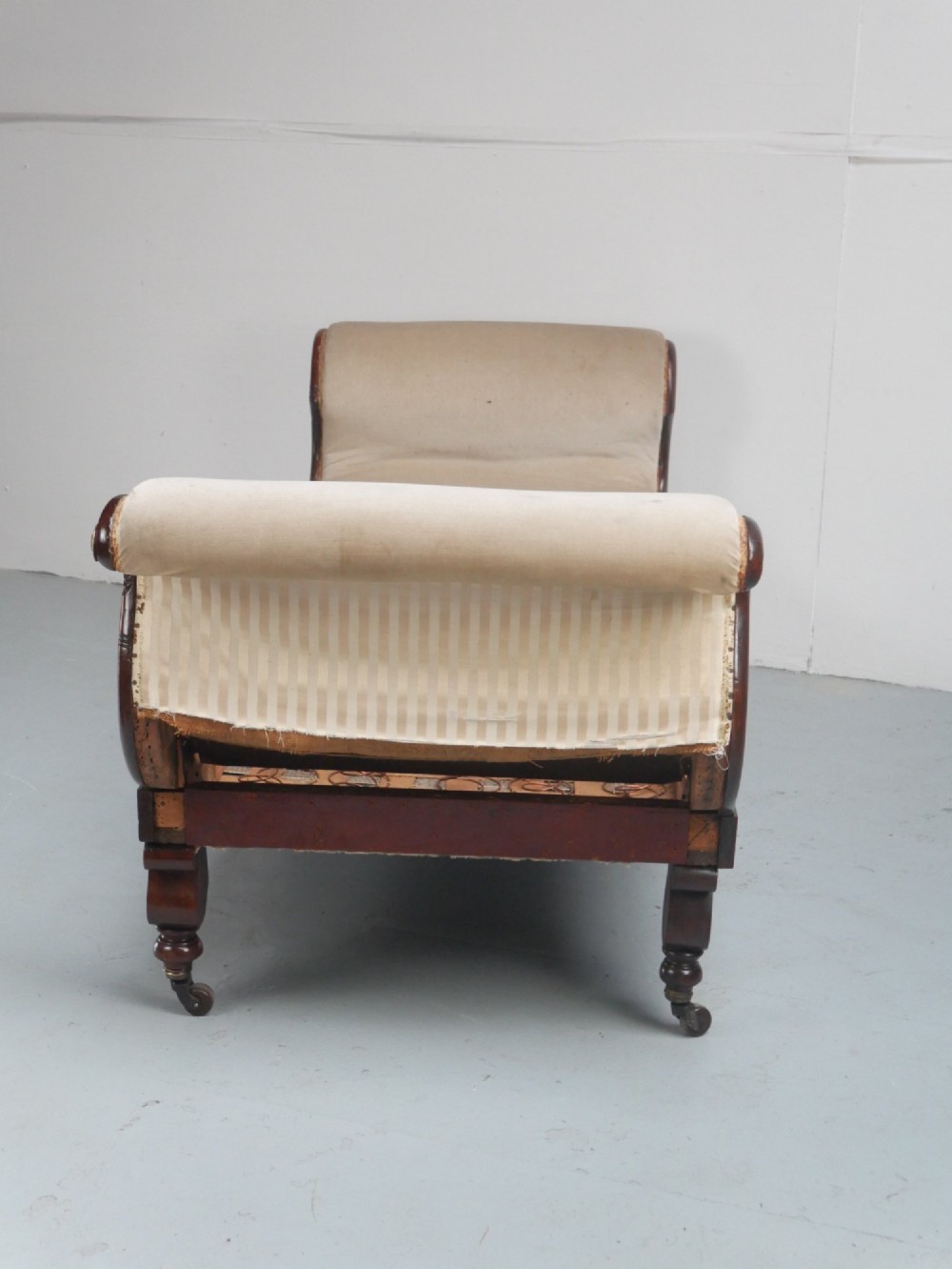 An early nineteenth-century Regency mahogany scroll-ended sofa frame featuring brass mounts, reeded turned legs on brass castors, and upholstered end scrolls with exposed spring seating. View IX