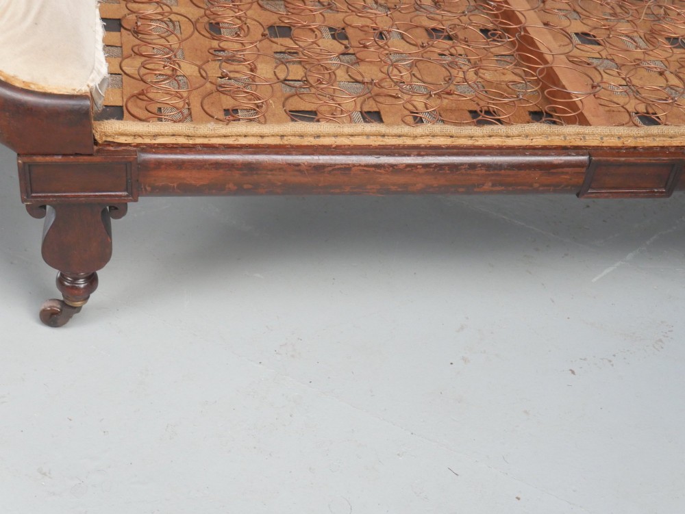 An early nineteenth-century Regency mahogany scroll-ended sofa frame featuring brass mounts, reeded turned legs on brass castors, and upholstered end scrolls with exposed spring seating. View XII