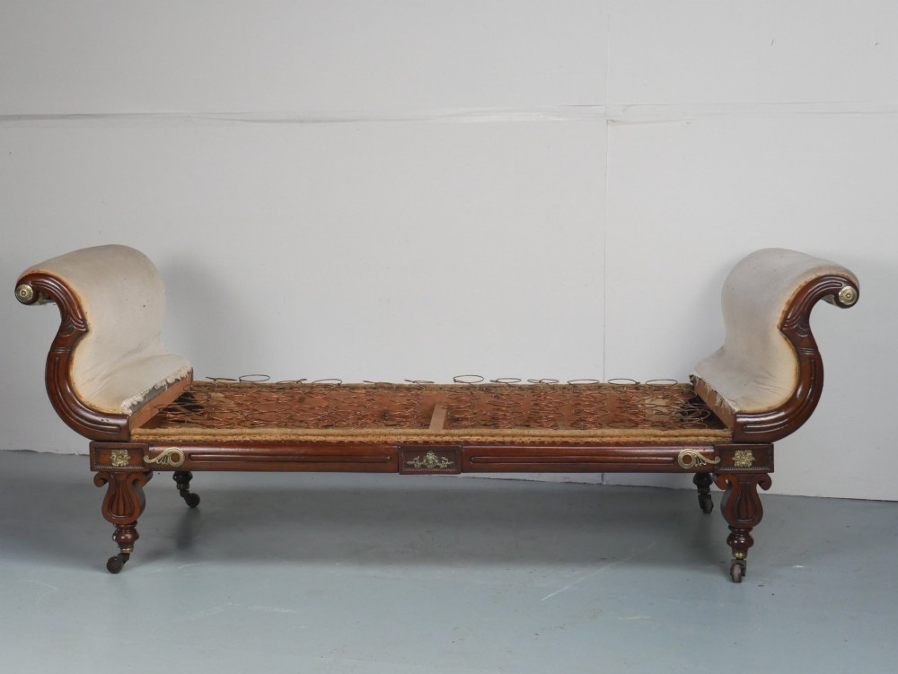 An early nineteenth-century Regency mahogany scroll-ended sofa frame featuring brass mounts, reeded turned legs on brass castors, and upholstered end scrolls with exposed spring seating. View XIII
