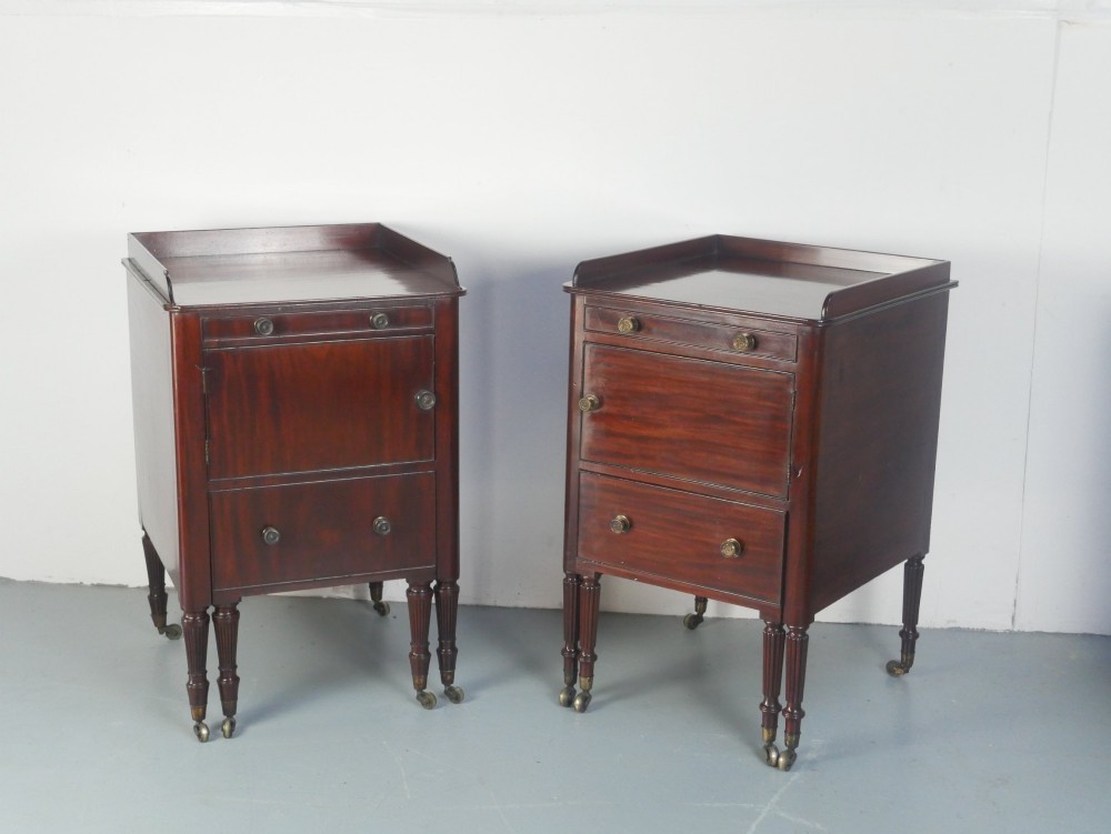 A matched pair of dark mahogany Regency bedside cupboards featuring gallery tops, single cupboard doors, lower drawers, reeded legs, and brass castors.