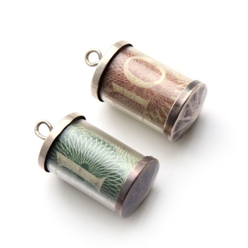 fig 1. A pair of cylindrical sterling silver charms enclosing a rolled green one pound note and a red ten shilling note.