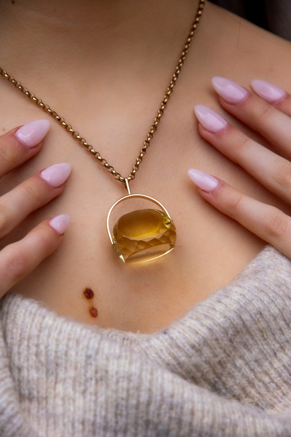 A large faceted yellow citrine gemstone held within an arched gold frame that pivots on a chain.
