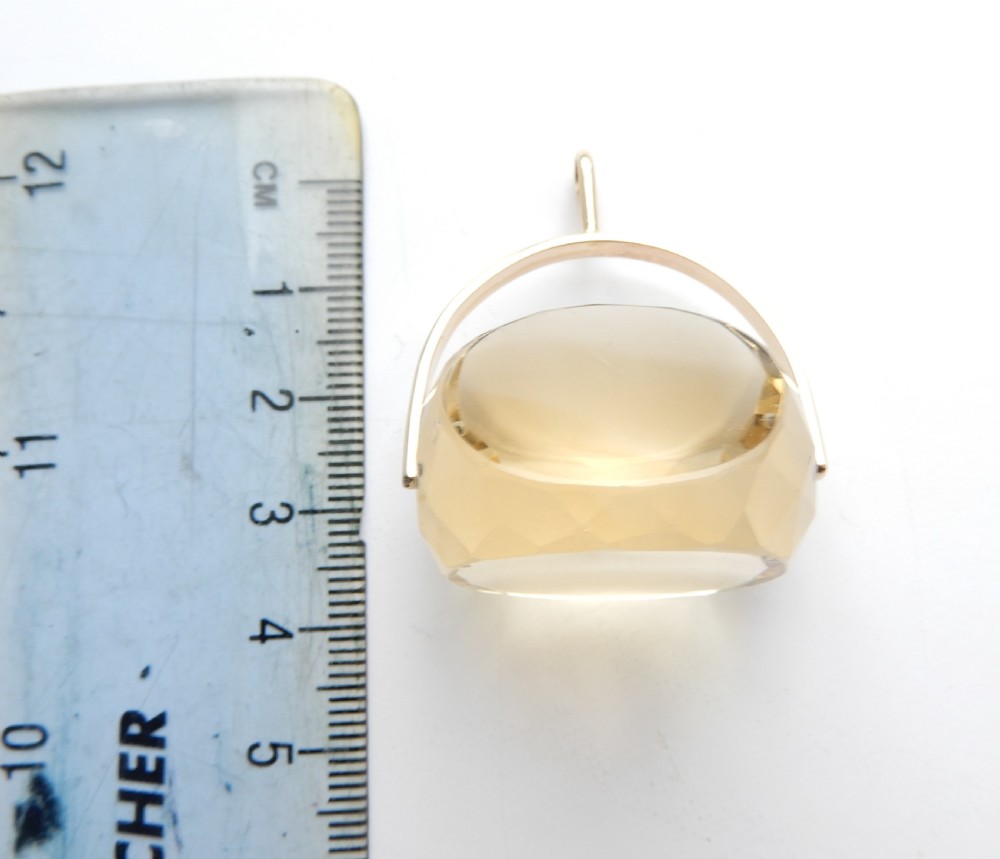 A large faceted yellow citrine gemstone held within an arched gold frame that pivots on a chain. View V