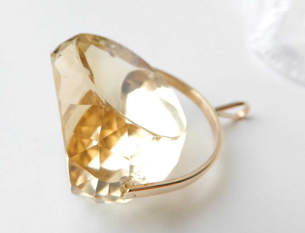 A large faceted yellow citrine gemstone held within an arched gold frame that pivots on a chain. View VI