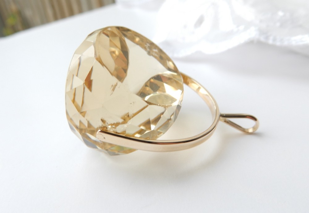 A large faceted yellow citrine gemstone held within an arched gold frame that pivots on a chain. View VII