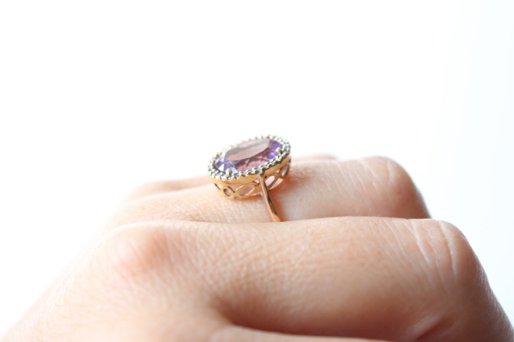 An antique 9ct gold ring featuring a large oval faceted purple amethyst surrounded by a halo of small white diamonds. View V