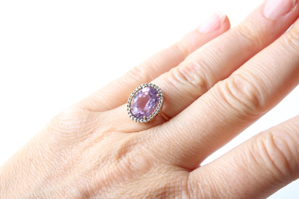 An antique 9ct gold ring featuring a large oval faceted purple amethyst surrounded by a halo of small white diamonds. View VI
