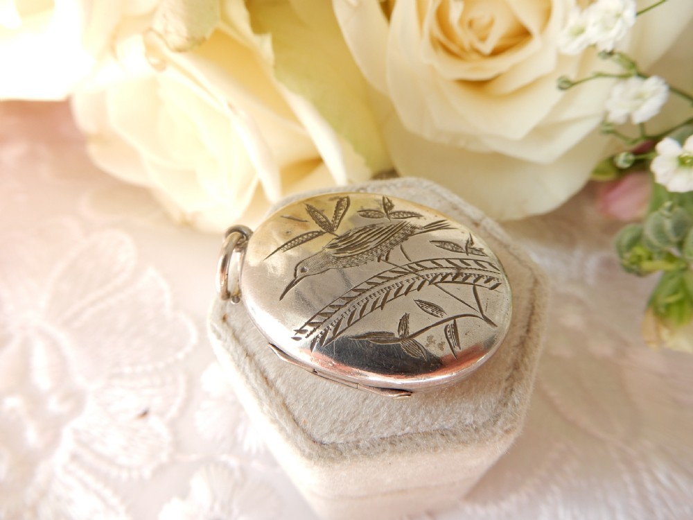 An oval sterling silver locket featuring a hand-engraved bird perched on foliage.