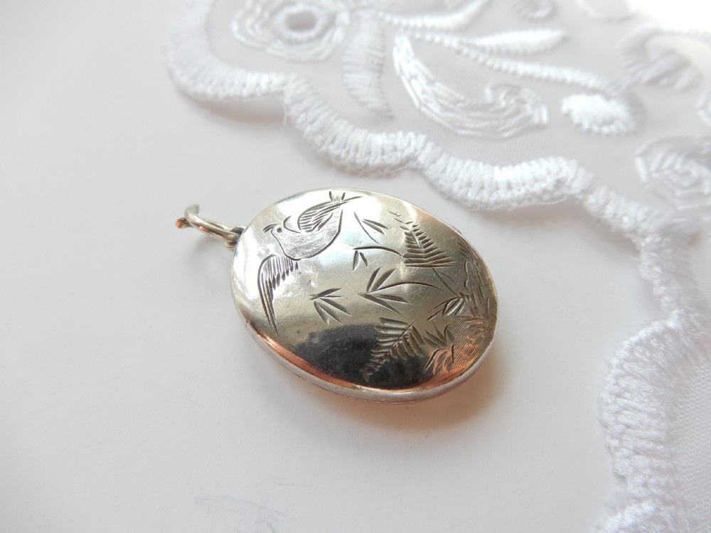 An oval sterling silver locket featuring a hand-engraved bird perched on foliage. View II