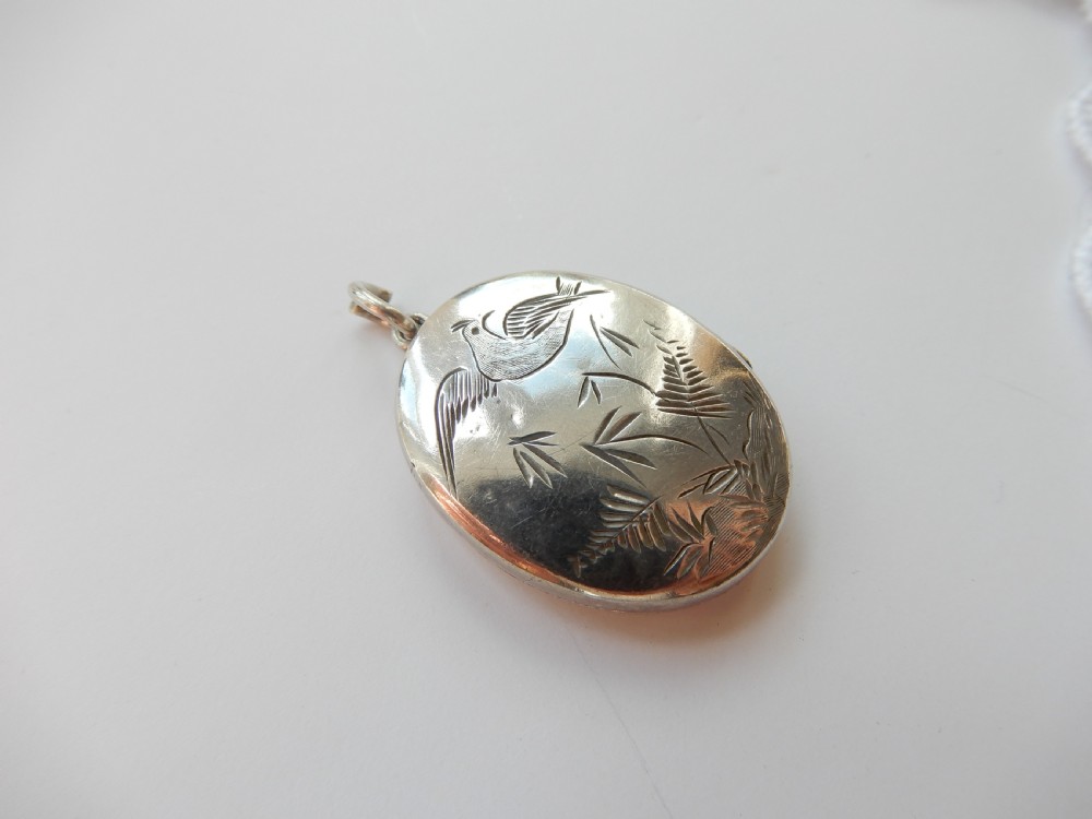 An oval sterling silver locket featuring a hand-engraved bird perched on foliage. View III