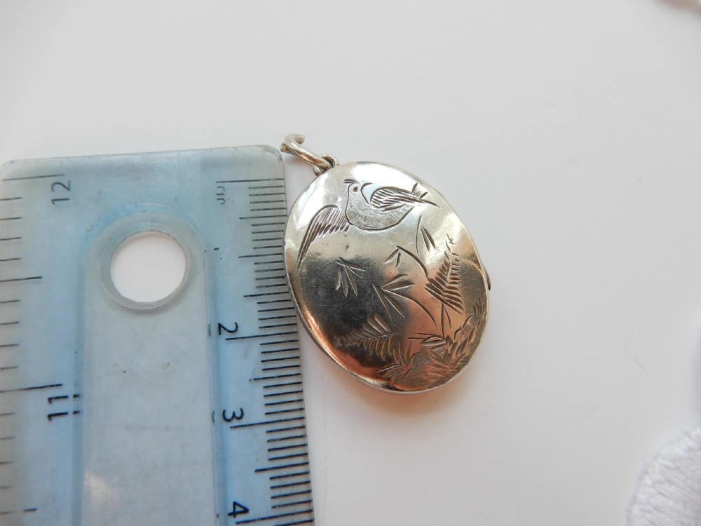 An oval sterling silver locket featuring a hand-engraved bird perched on foliage. View IV