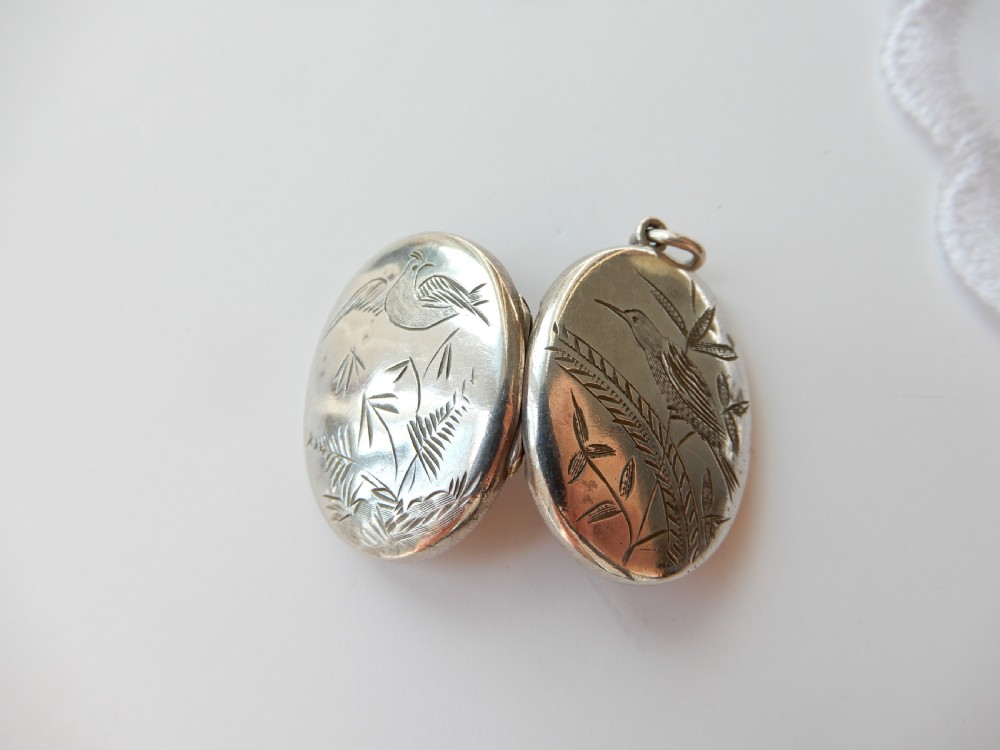 An oval sterling silver locket featuring a hand-engraved bird perched on foliage. View VI