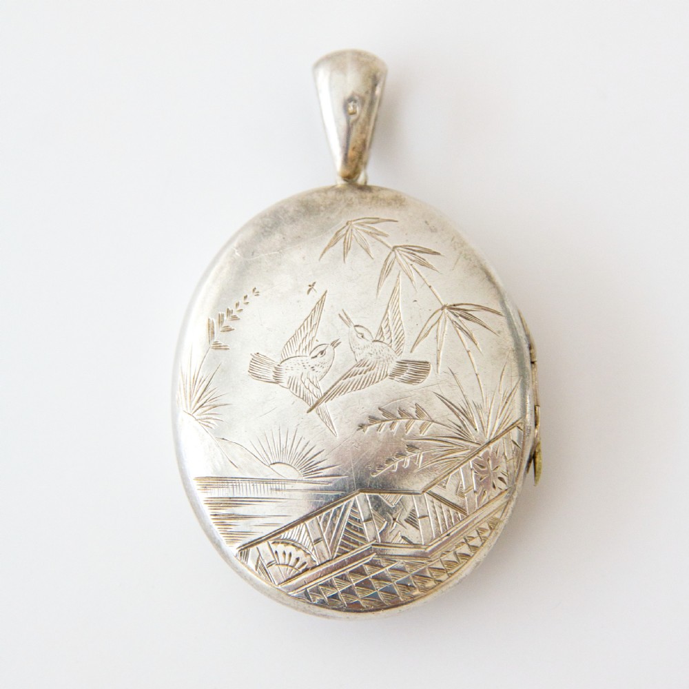 An oval silver locket featuring hand-engraved decoration of two birds, bamboo leaves, a sunburst motif, and geometric patterns.