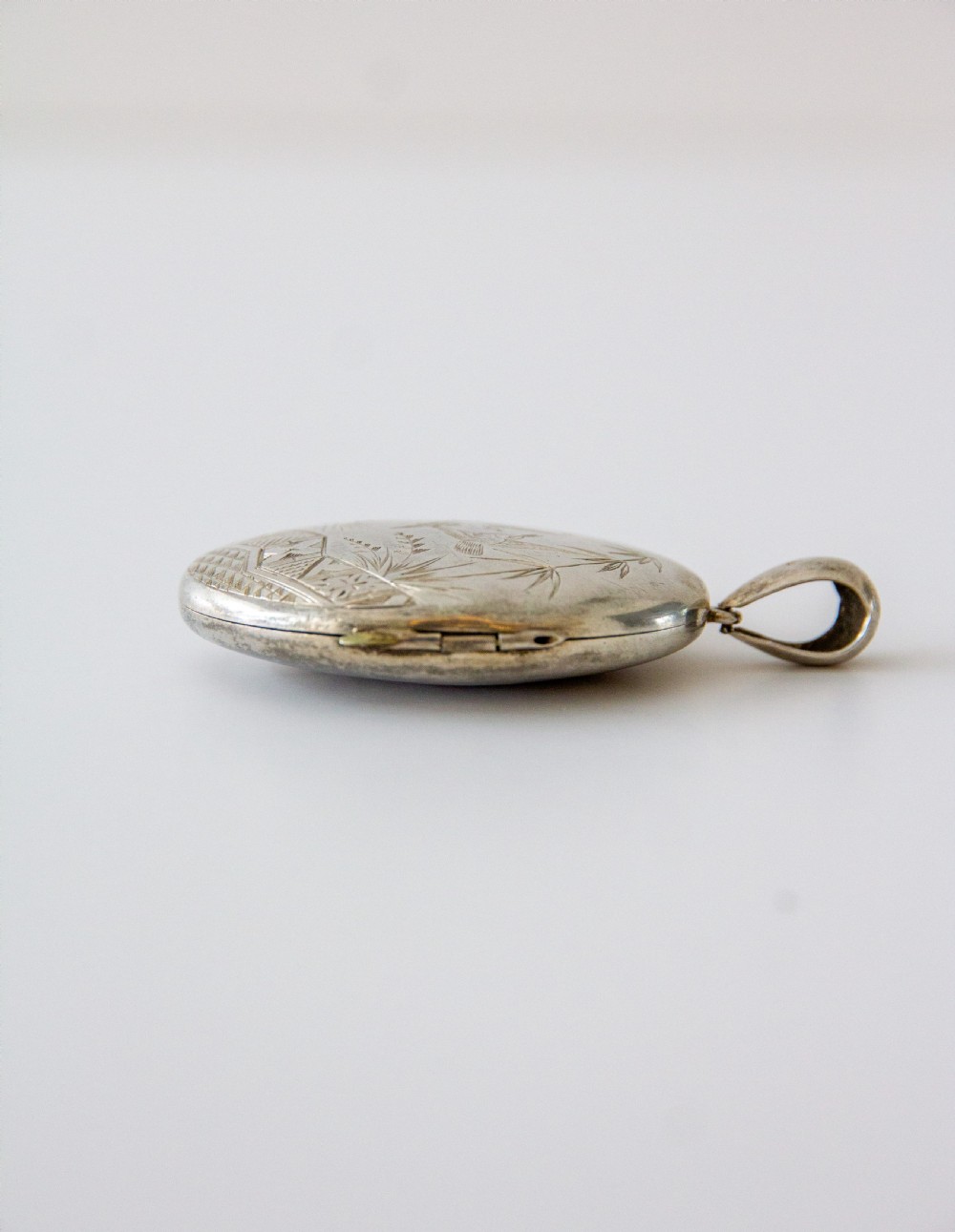 An oval silver locket featuring hand-engraved decoration of two birds, bamboo leaves, a sunburst motif, and geometric patterns. View IV