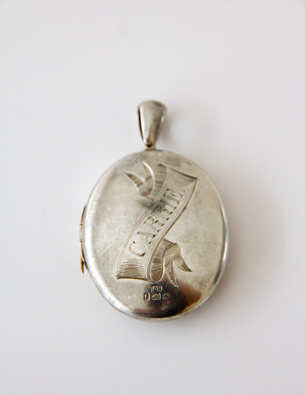 An oval silver locket featuring hand-engraved decoration of two birds, bamboo leaves, a sunburst motif, and geometric patterns. View V