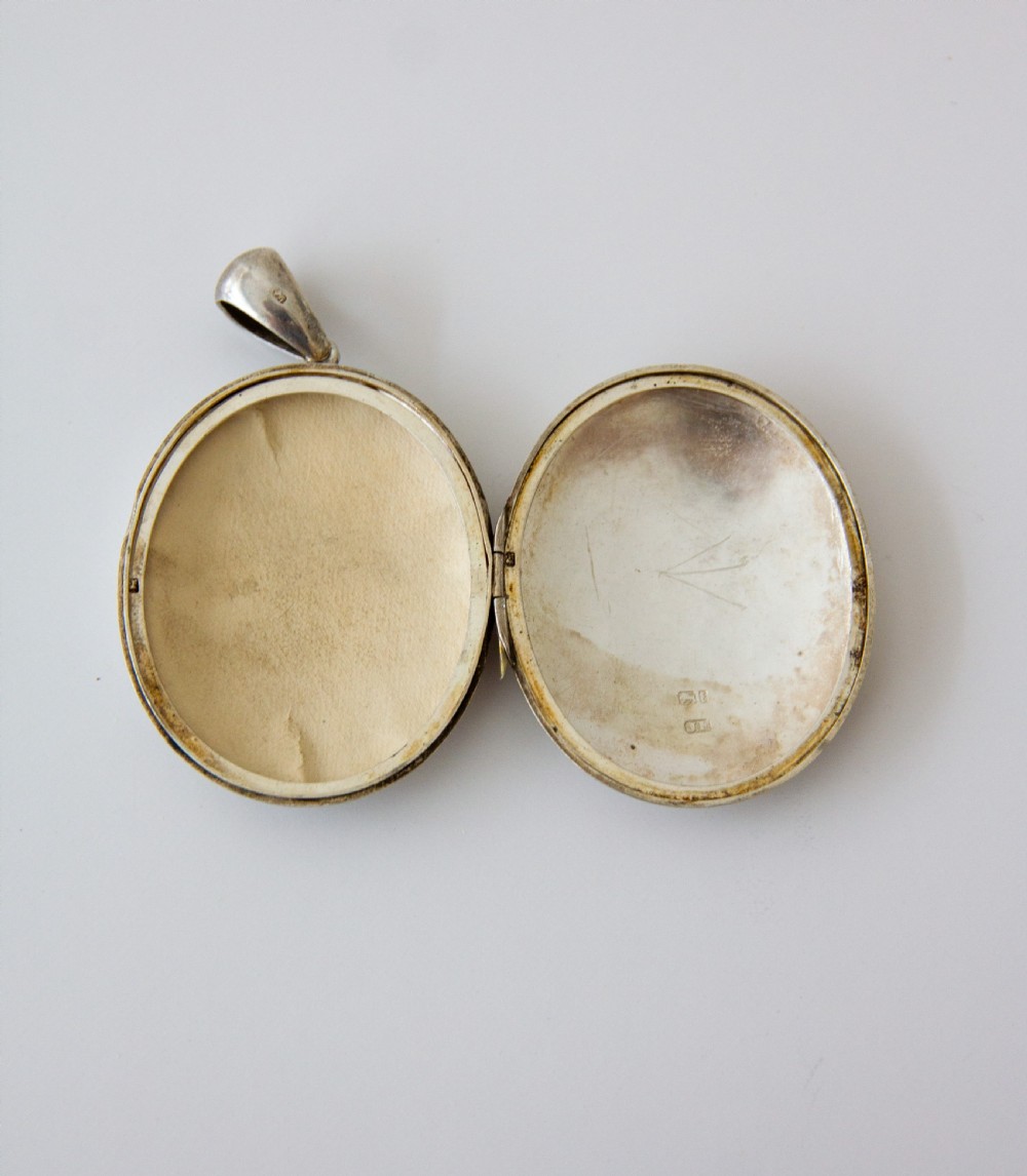 An oval silver locket featuring hand-engraved decoration of two birds, bamboo leaves, a sunburst motif, and geometric patterns. View VI