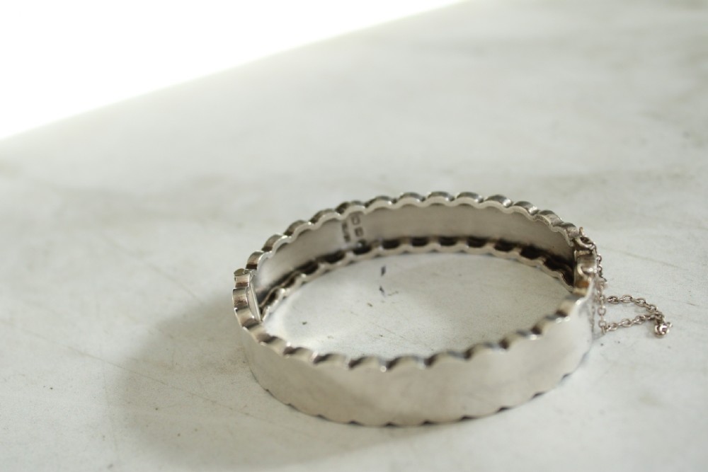 Victorian sterling silver hinged bangle with scalloped borders and applied foliate engraving. View II