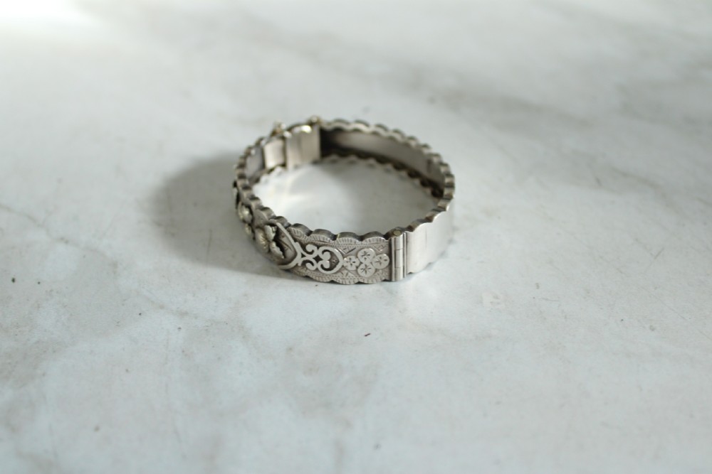 Victorian sterling silver hinged bangle with scalloped borders and applied foliate engraving. View V