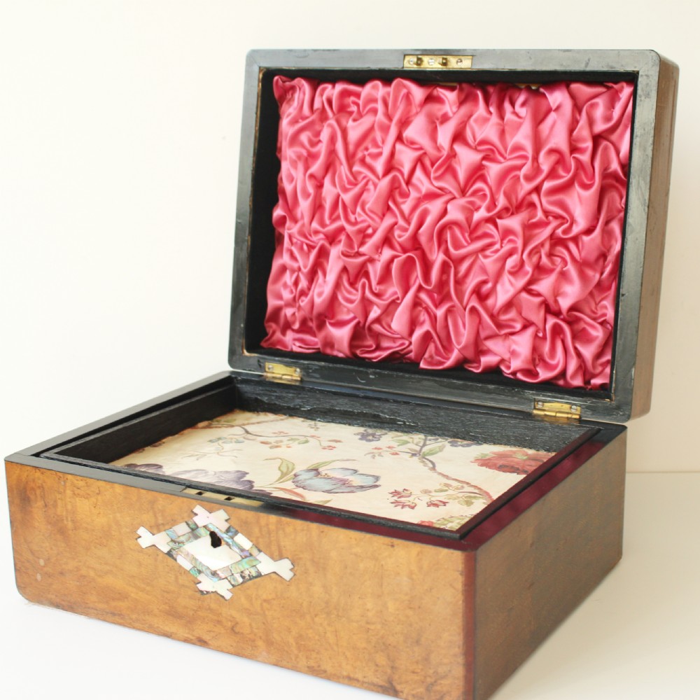 An open hinged walnut wooden box featuring a diamond-shaped mother-of-pearl inlay around the front keyhole, a pink ruched silk lid interior, and a floral fabric lined tray base.