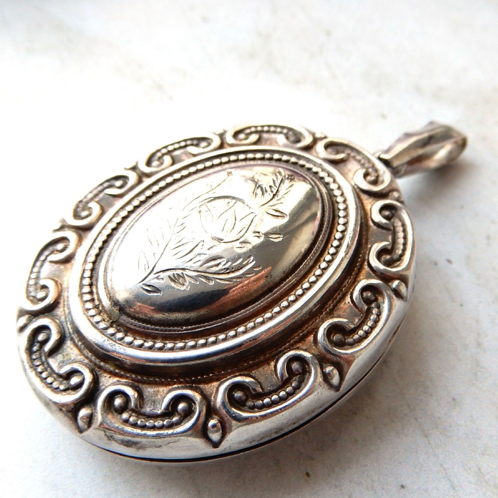 A large oval Victorian sterling silver locket featuring engraved foliage and a scrollwork border.