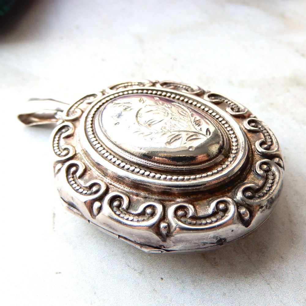 A large oval Victorian sterling silver locket featuring engraved foliage and a scrollwork border. View IV