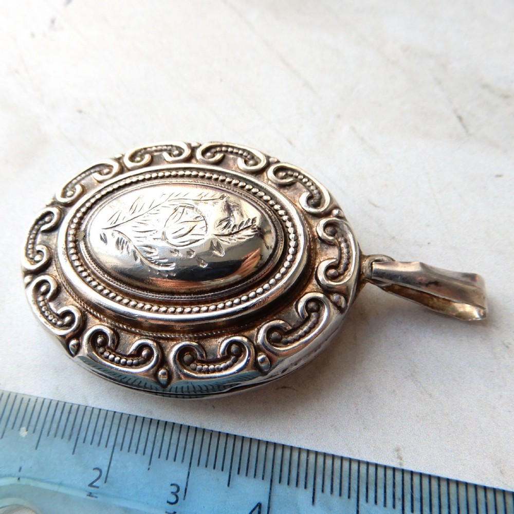 A large oval Victorian sterling silver locket featuring engraved foliage and a scrollwork border. View V