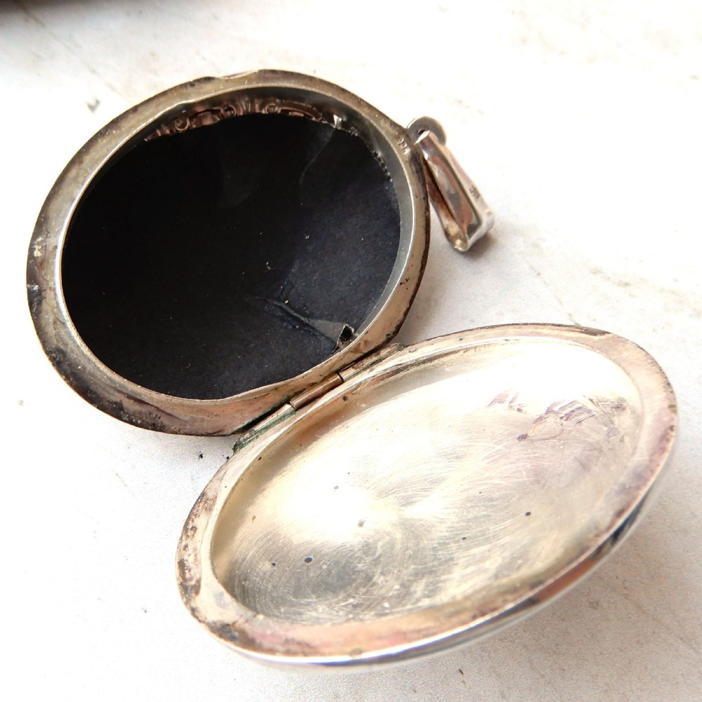 A large oval Victorian sterling silver locket featuring engraved foliage and a scrollwork border. View VI