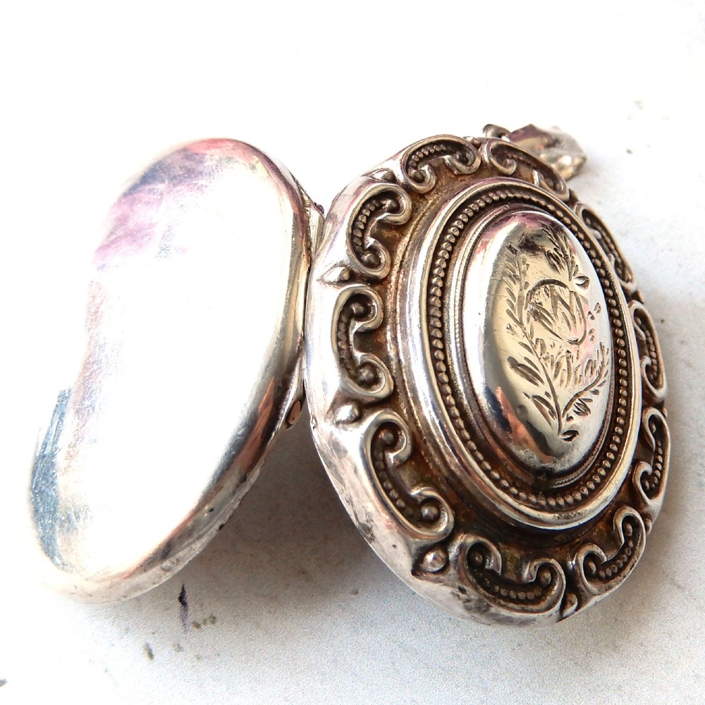 A large oval Victorian sterling silver locket featuring engraved foliage and a scrollwork border. View VII