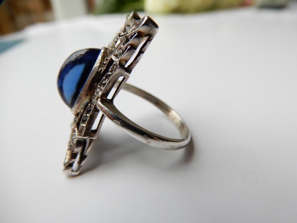 An Art Deco silver navette ring featuring an oval blue paste cabochon surrounded by clear paste stones in a geometric filigree setting. View VI