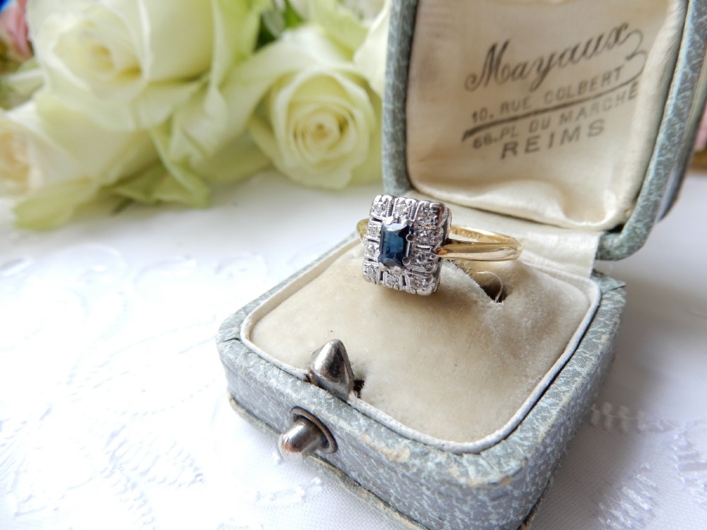 An Art Deco ring featuring a central rectangular blue sapphire surrounded by a geometric halo of small diamonds set in platinum atop an 18ct yellow gold band. View II