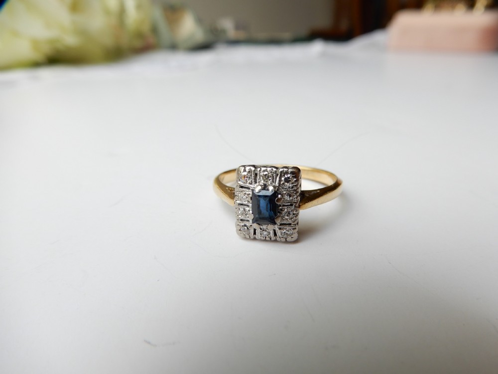 An Art Deco ring featuring a central rectangular blue sapphire surrounded by a geometric halo of small diamonds set in platinum atop an 18ct yellow gold band. View III