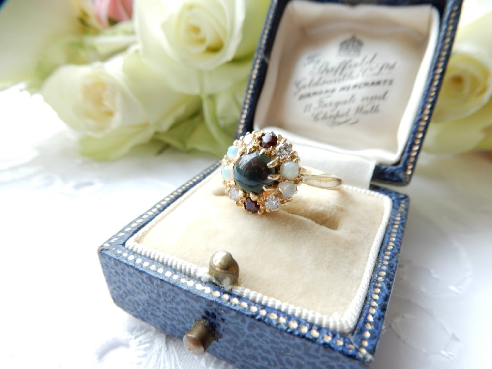 An antique yellow gold cluster ring set with a central cabochon bloodstone surrounded by alternating opals, garnets, and diamonds.