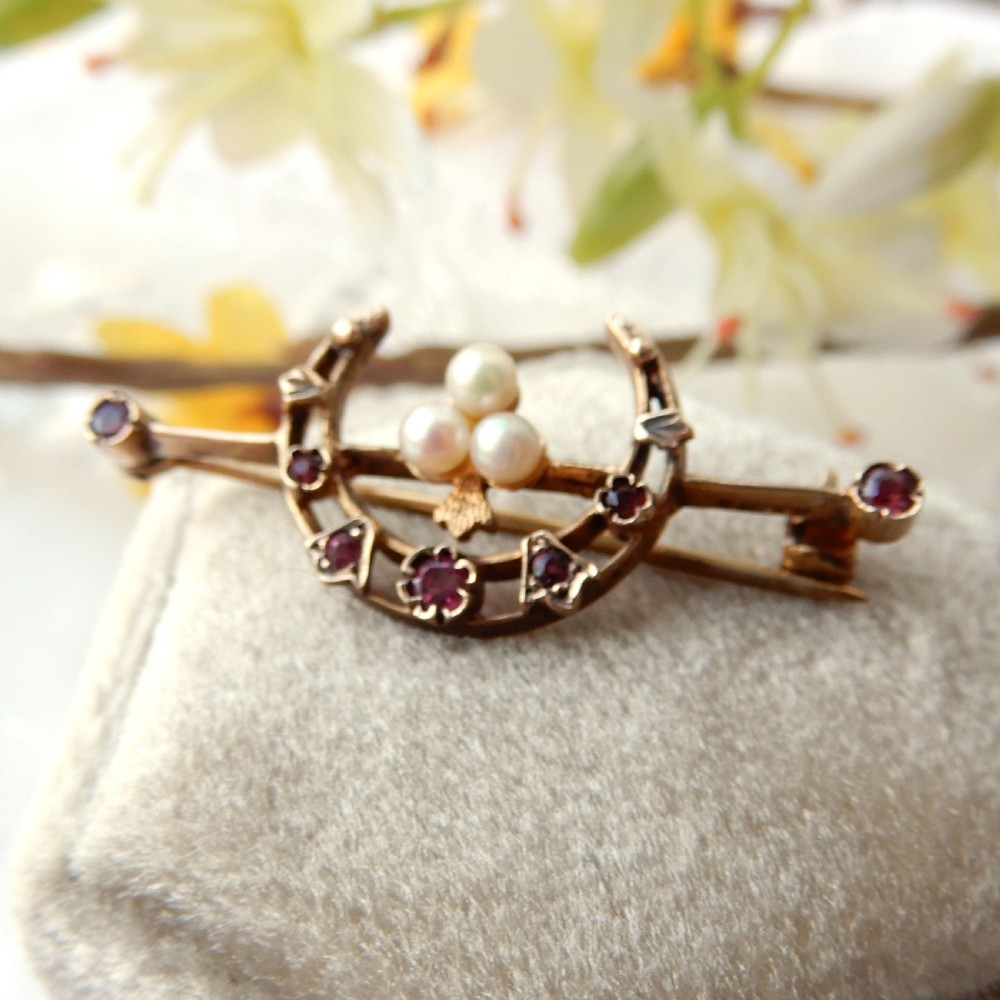 An antique 9ct gold bar brooch featuring a central crescent motif set with rubies and three seed pearls.