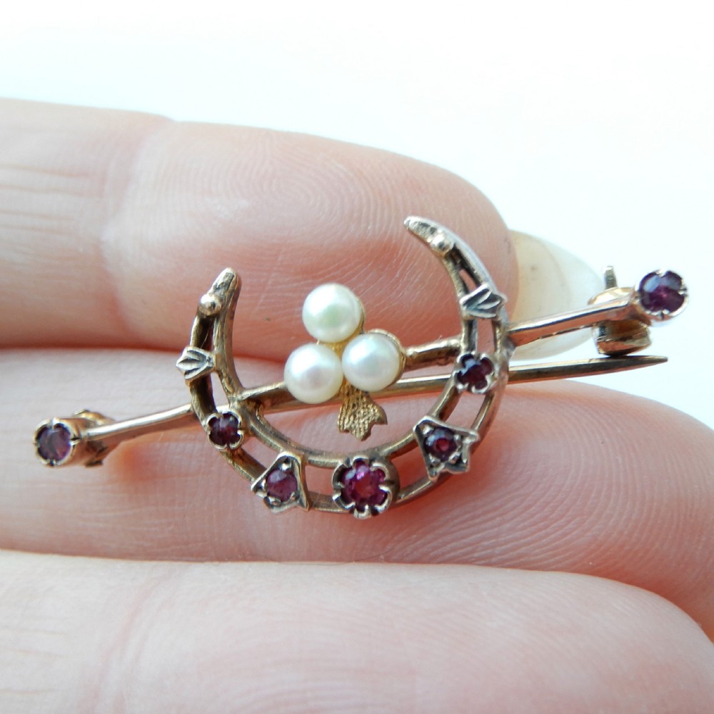 An antique 9ct gold bar brooch featuring a central crescent motif set with rubies and three seed pearls. View II