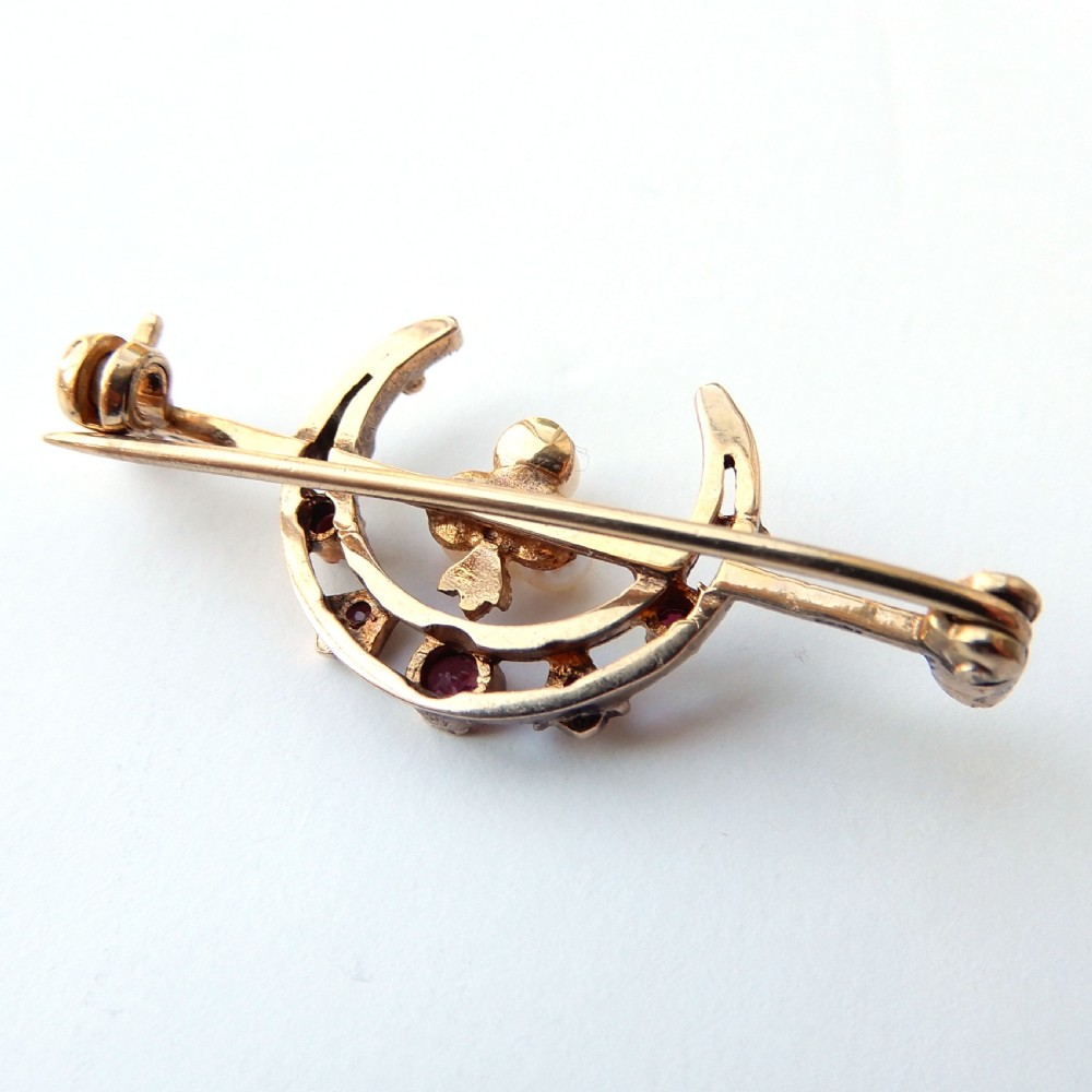 An antique 9ct gold bar brooch featuring a central crescent motif set with rubies and three seed pearls. View VI