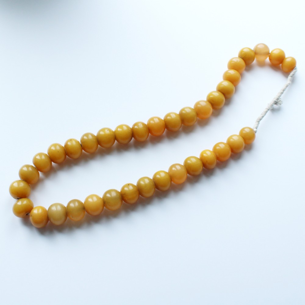 A continuous strand of smooth, round butterscotch yellow Bakelite beads strung on thread against a plain white background.