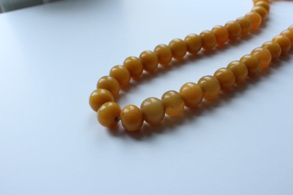 A continuous strand of smooth, round butterscotch yellow Bakelite beads strung on thread against a plain white background. View II