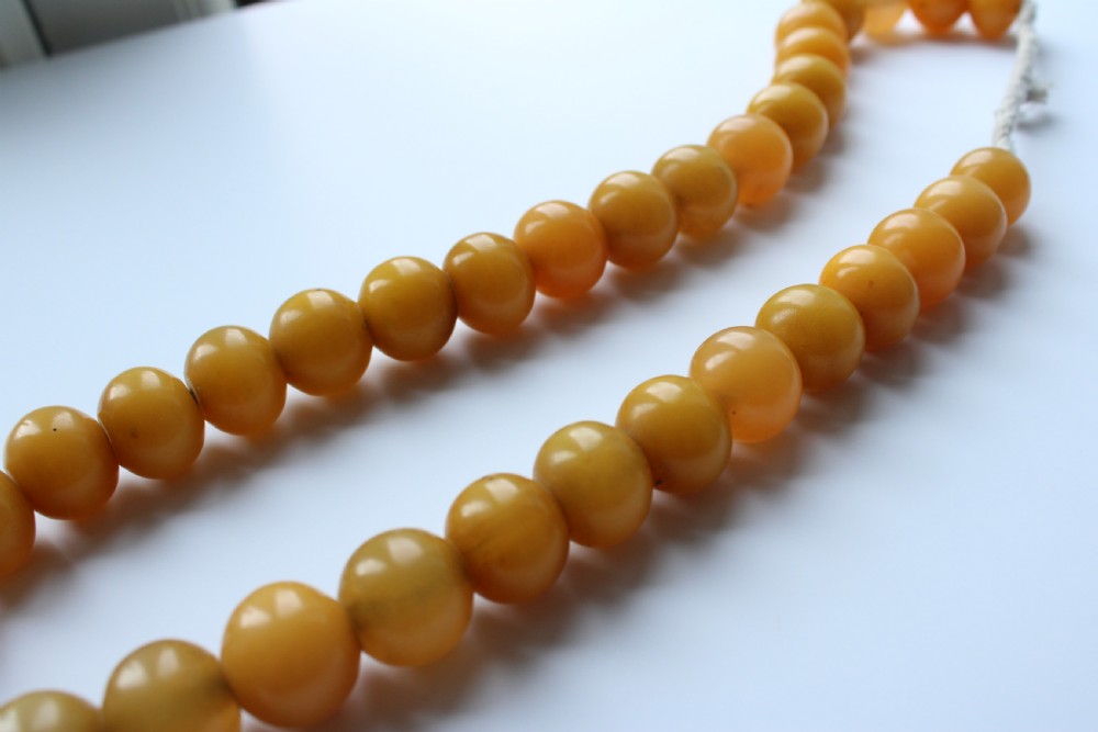 A continuous strand of smooth, round butterscotch yellow Bakelite beads strung on thread against a plain white background. View III